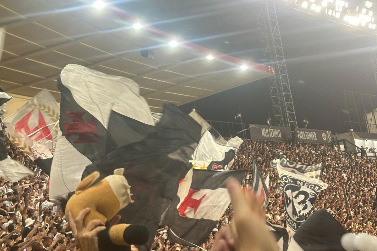 Torcida do Vasco agitando bandeiras com a Cruz de Malta na arquibancada lotada de São Januário em jogo noturno
