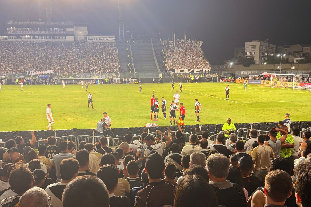 Jogadores do Vasco em campo no gramado de São Januário vistos da arquibancada lotada durante jogo noturno