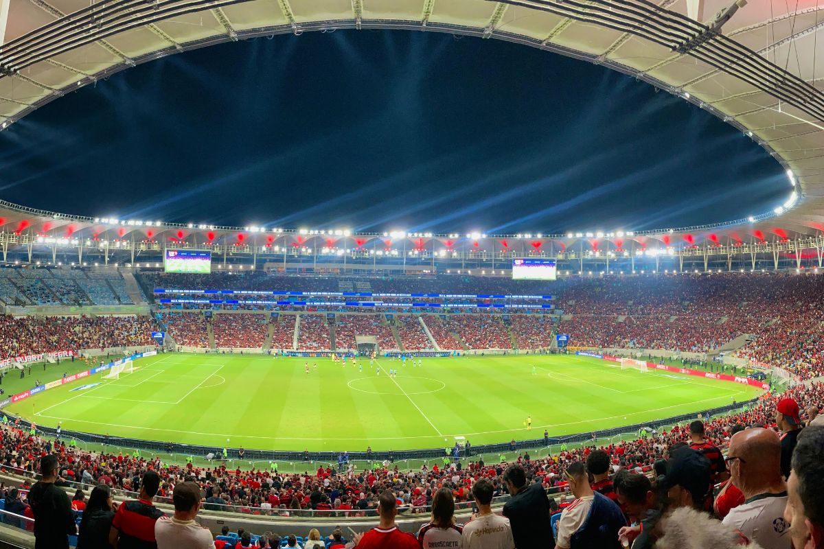 Vista panorâmica do Setor Leste Superior do Maracanã à noite, com o gramado iluminado e a torcida do Flamengo lotando as arquibancadas